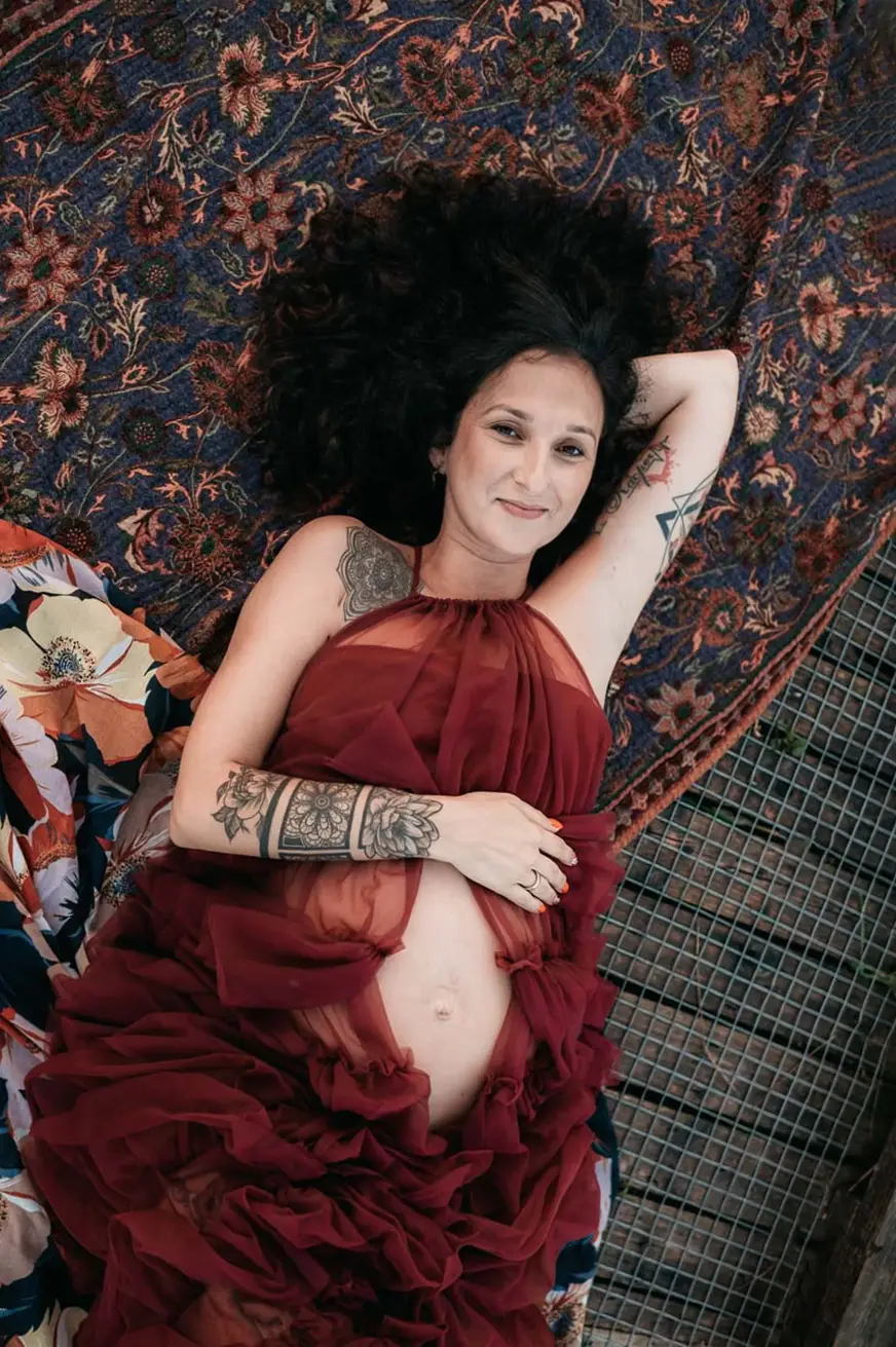 Kobieta w ciąży leżąca w czerwonej sukni podczas naturalnej sesji ciążowej w Krakowie