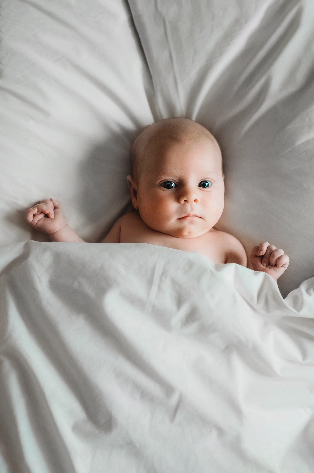 Noworodek leżący w łóżku przykryty kołdrą na poduszce podczas naturalnej sesji noworodkowej w Krakowie