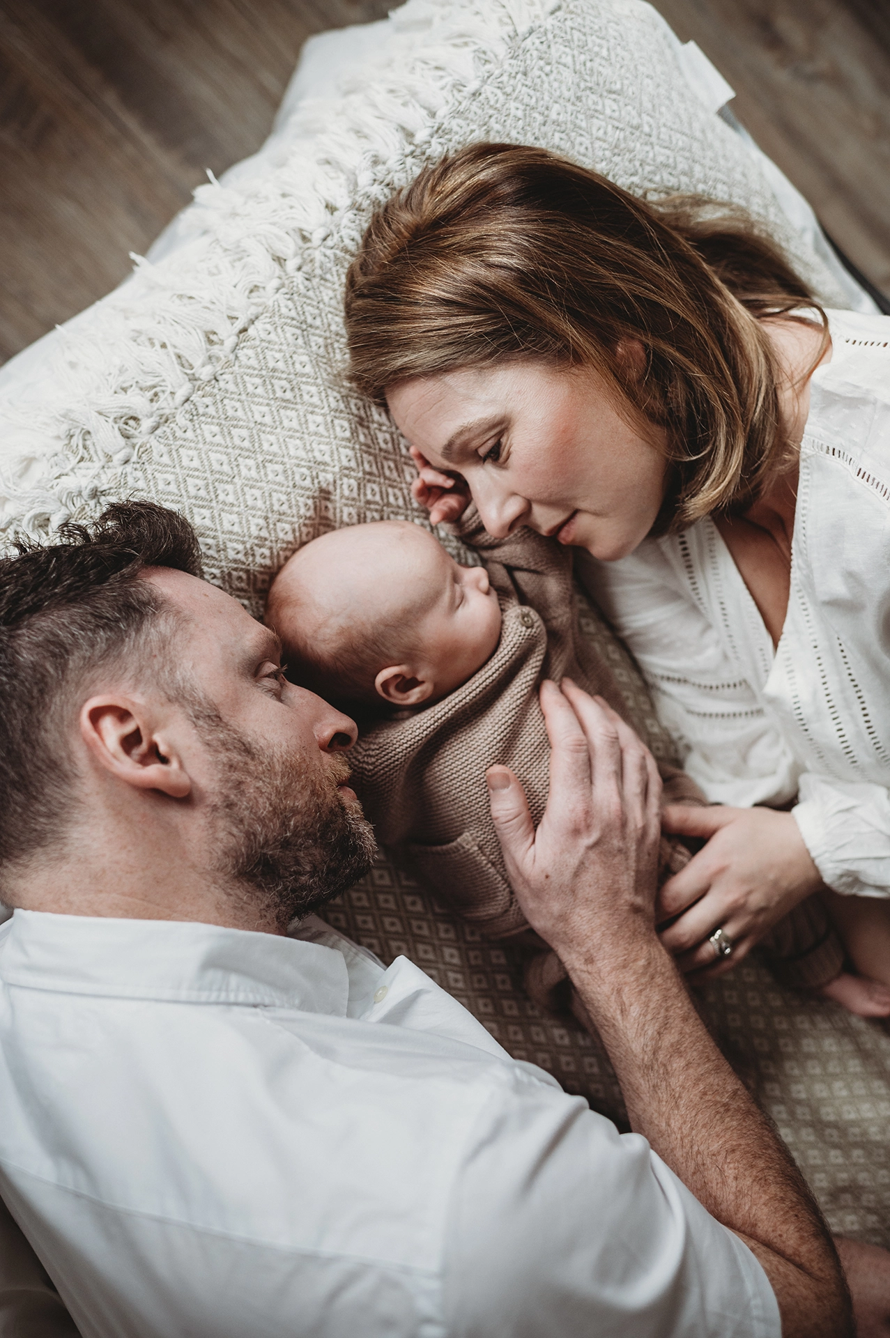 Rodzice z noworodkiem leżący razem podczas naturalnej sesji noworodkowej w domu w Krakowie