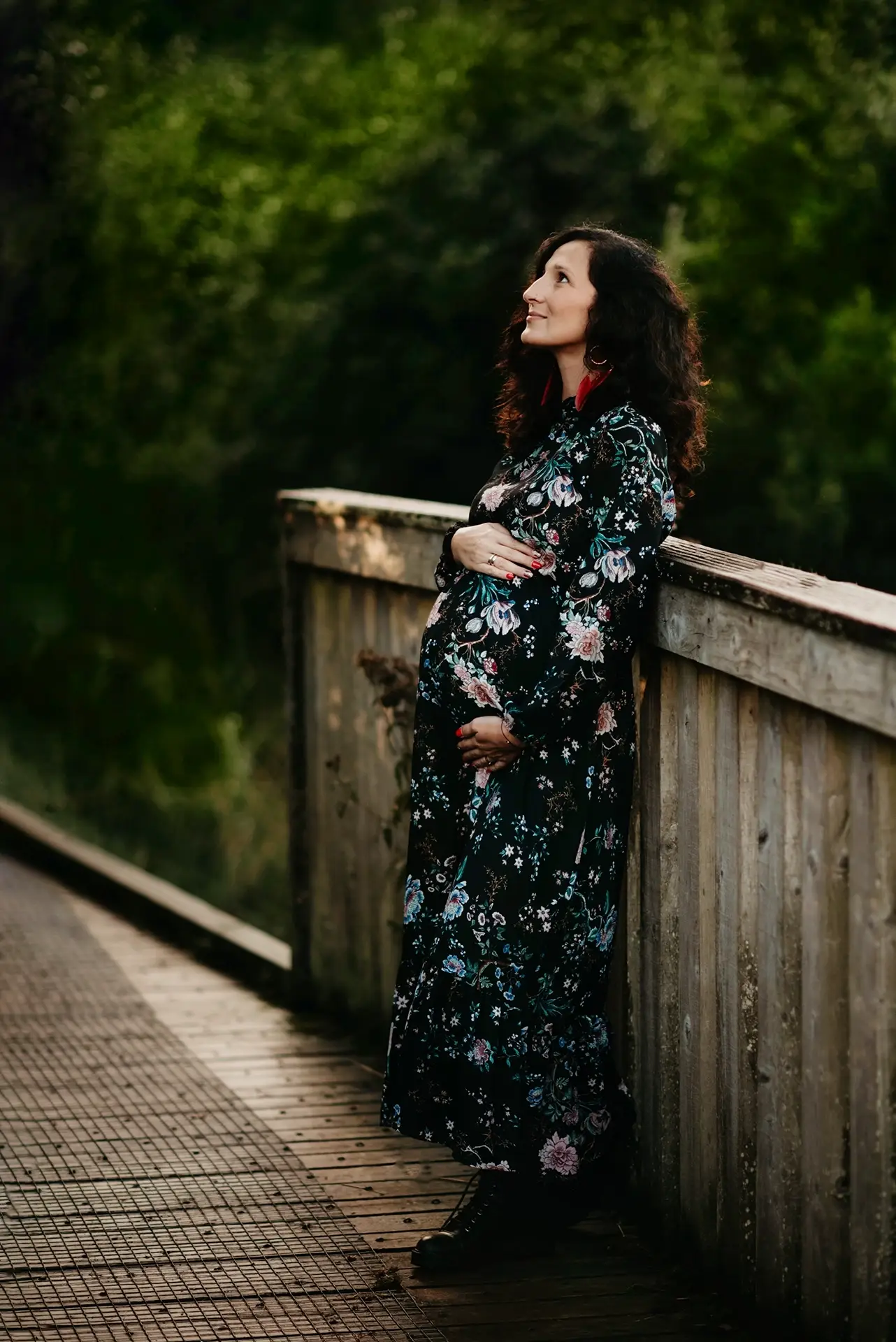 Kobieta w ciąży oparta o drewnianą barierkę podczas plenerowej sesji ciążowej w Krakowie